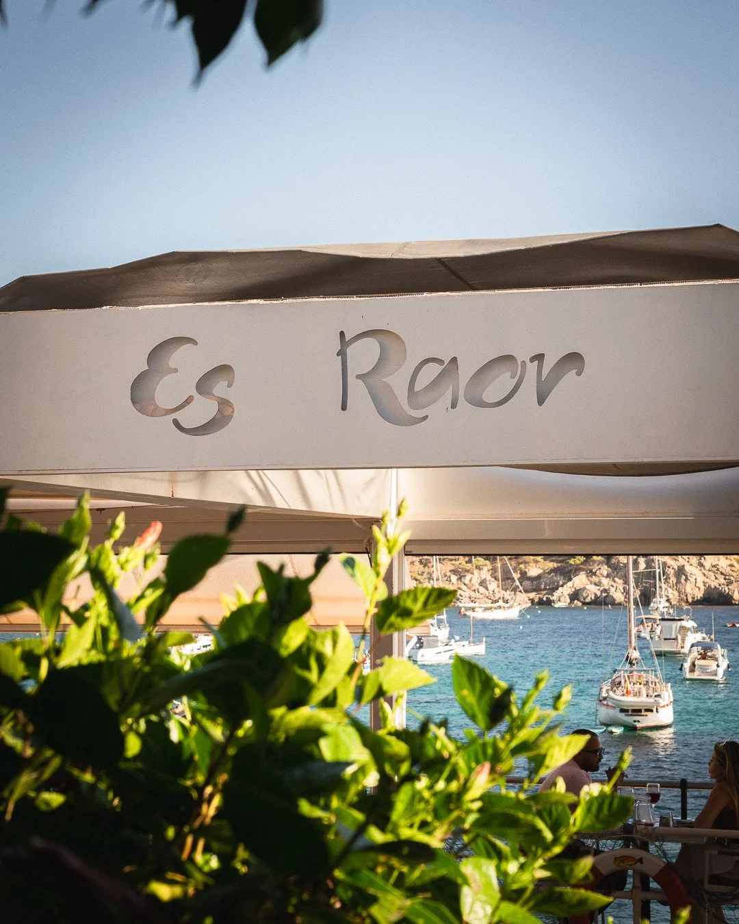 Una postal inolvidable del verano mallorquín. Bajo el distintivo toldo del Restaurante Es Raor en Sant Elm (Andratx), se abre un oasis gastronómico frente al mar. Enmarcada por la vegetación natural, nuestra terraza ofrece a los comensales una panorá