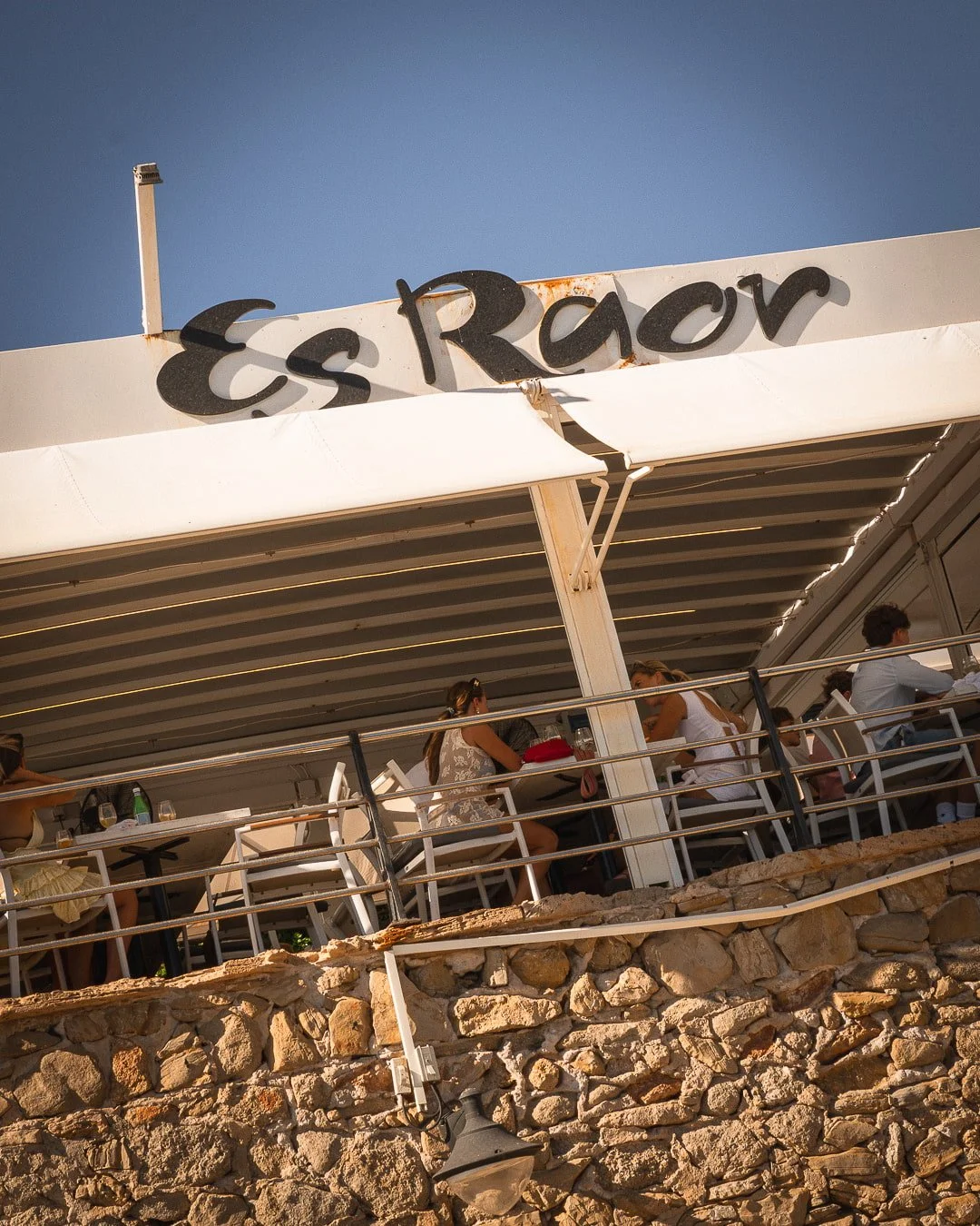 Reconocible al instante, la fachada del Restaurante Es Raor te da la bienvenida al corazón de Sant Elm (Andratx). Nuestra amplia terraza cubierta se alza sobre un robusto muro de piedra tradicional mallorquina, ofreciendo a nuestros comensales un esp