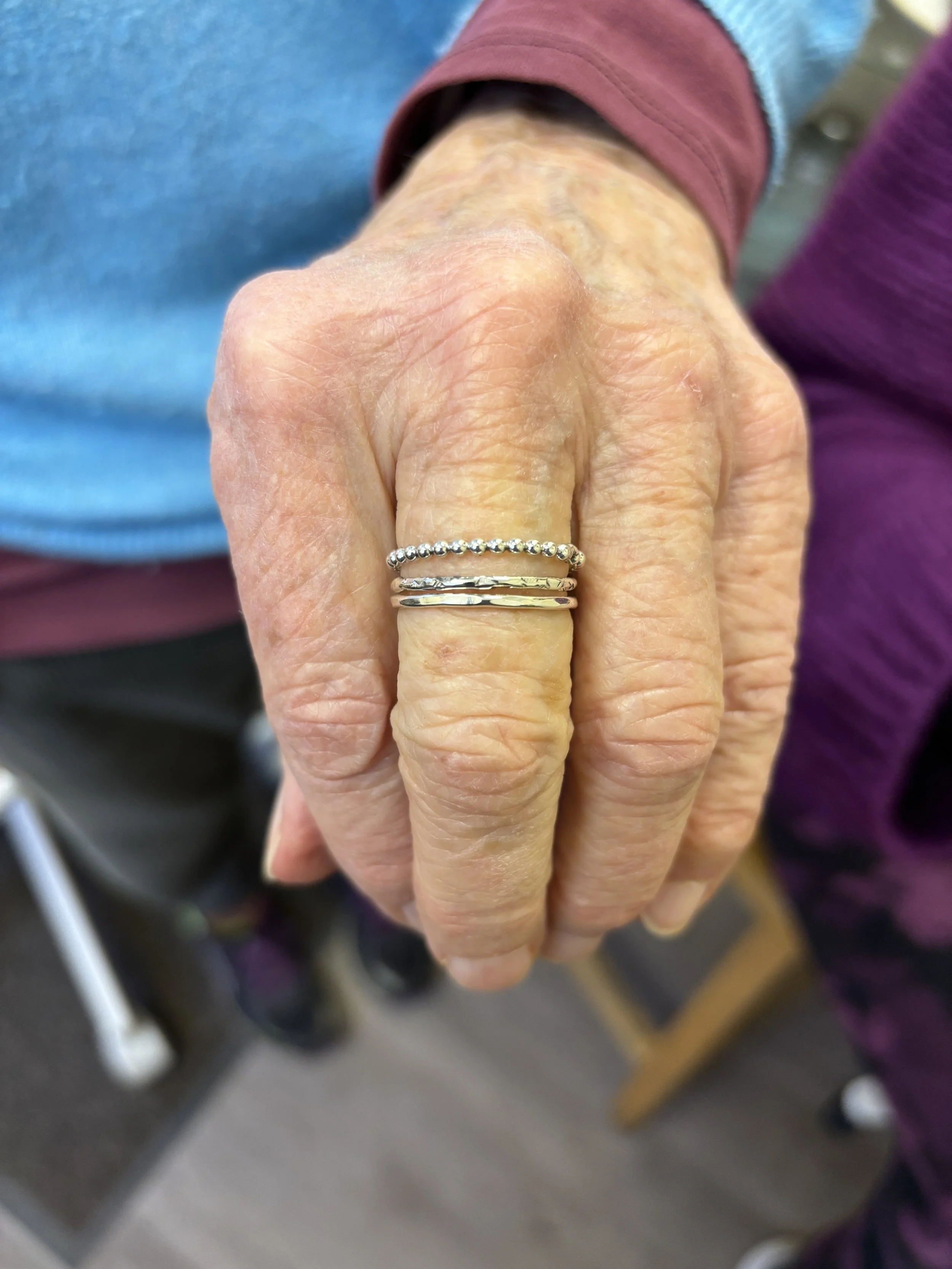 A ladies hand showing off her handmade recycled silver stacking ring set, three rings each with a different texture