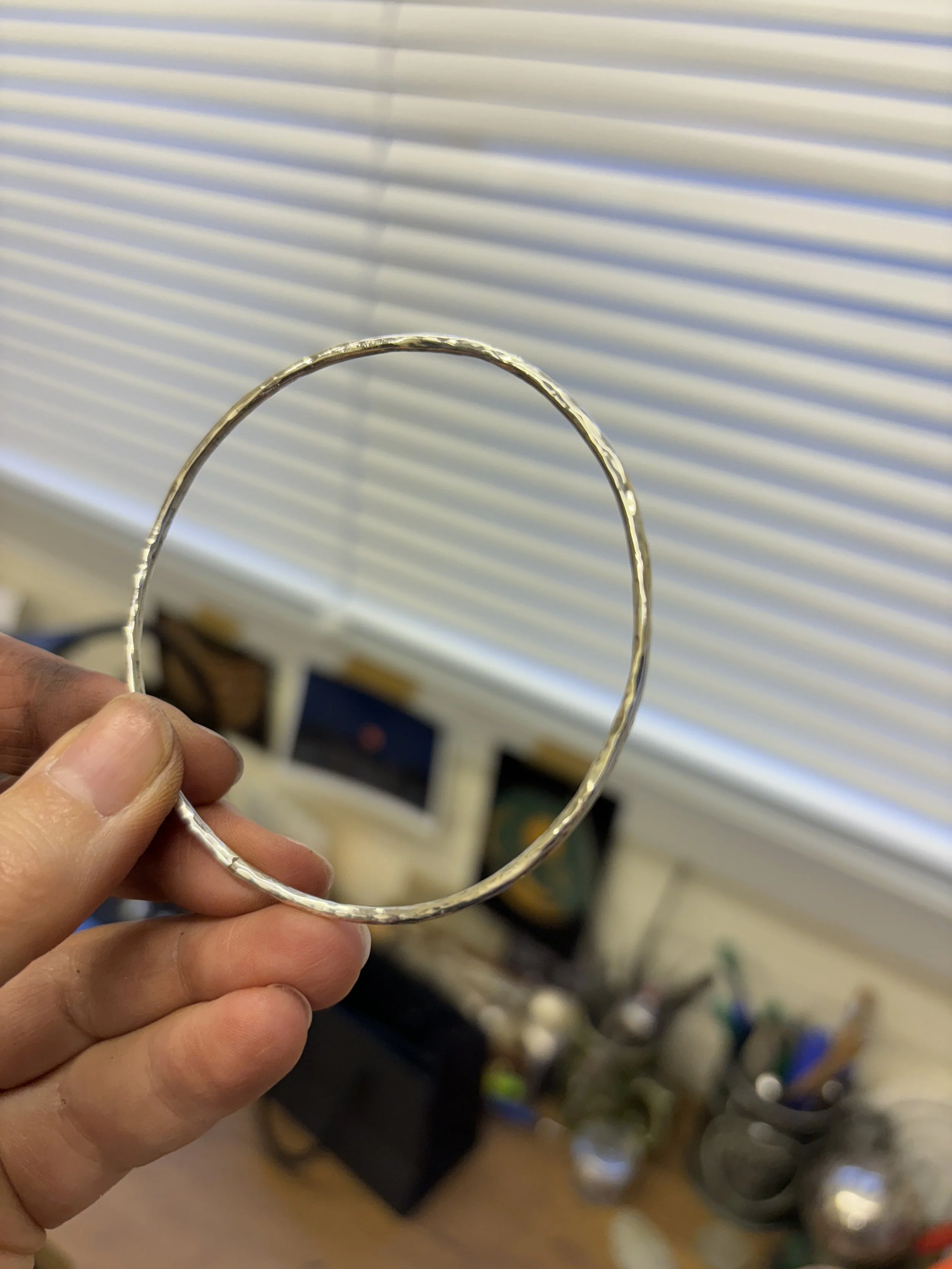 A recycled silver handmade bangle with reflective texture added by a hammer
