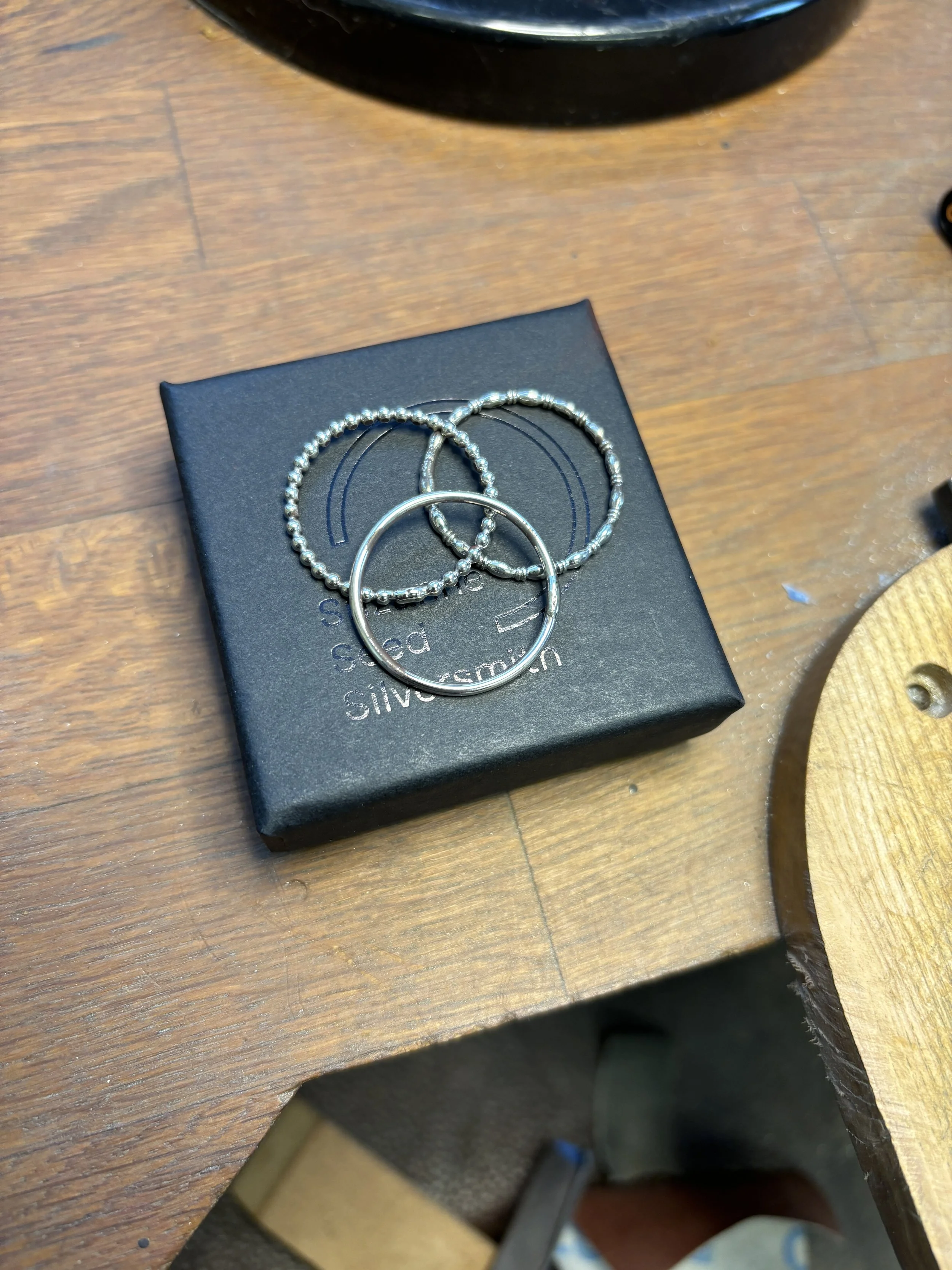 Set of three silver stacking rings with different textures, sat on top of a black box branded with Suzanne Seed Silversmith