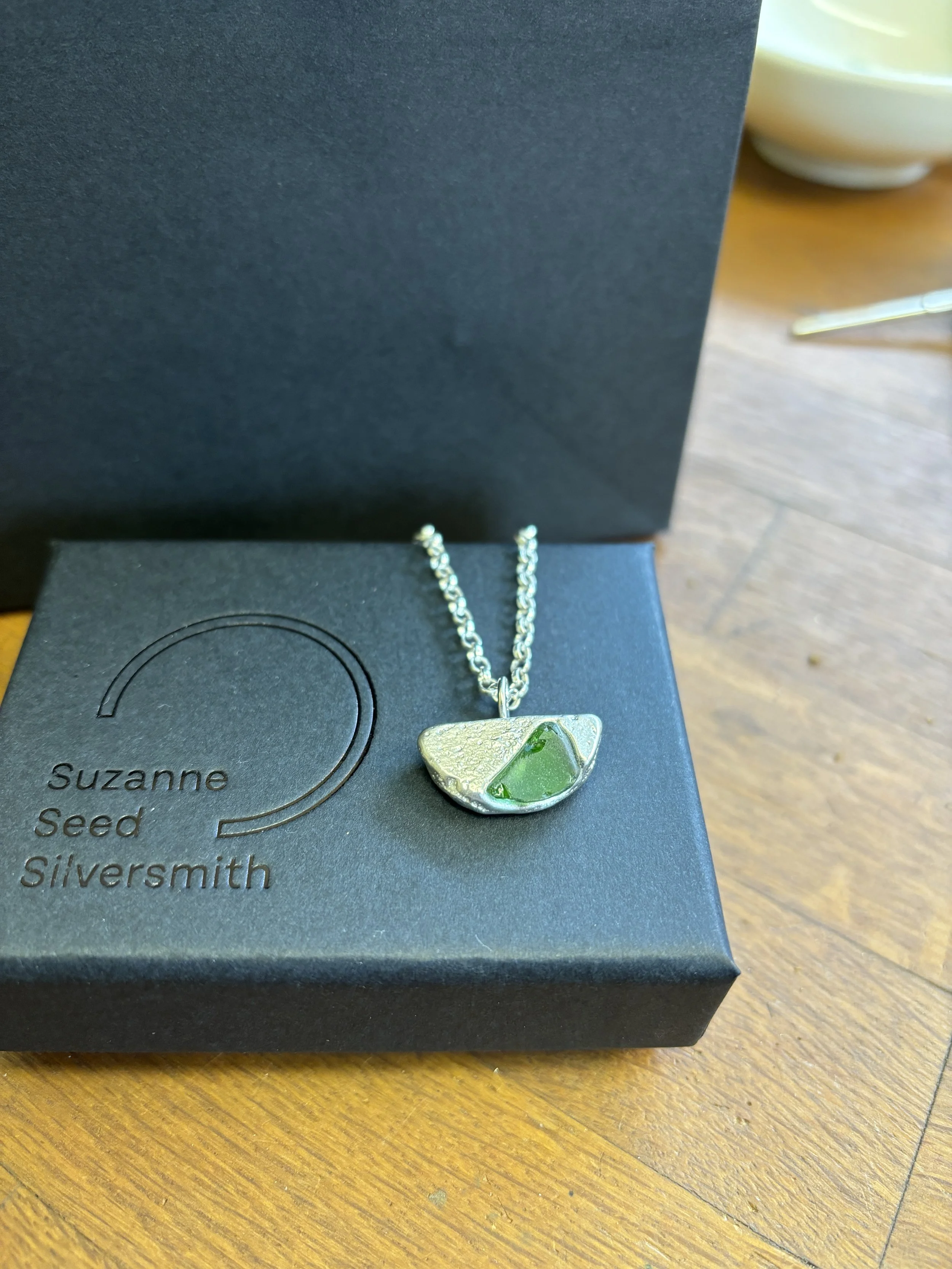 A recycled silver pendant and necklace with some seagrass set into the design