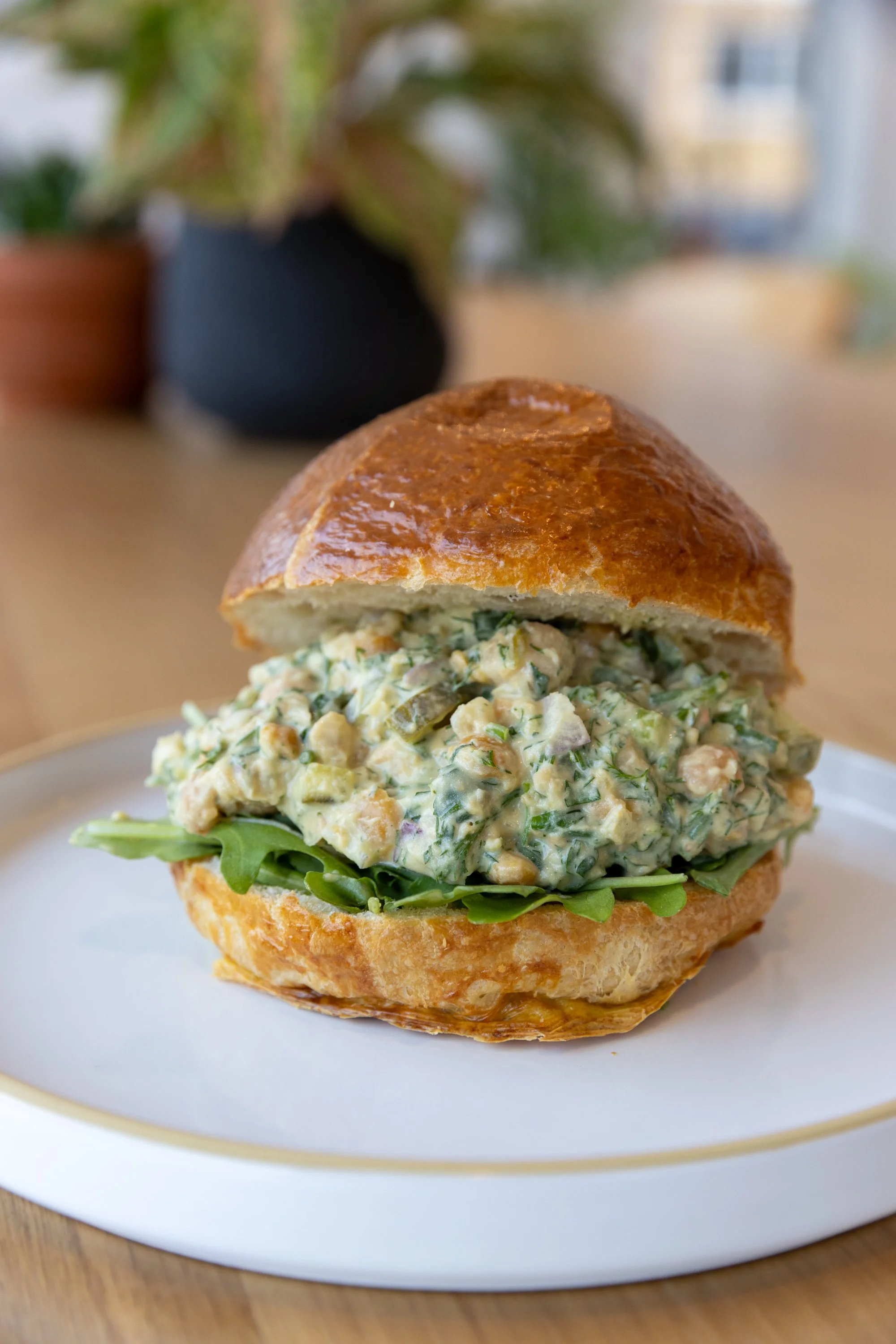 Close-up of a creamy vegan chickpea salad sandwich on a white plate showing the texture of the chickpea mix and a golden, vegan brioche bun.