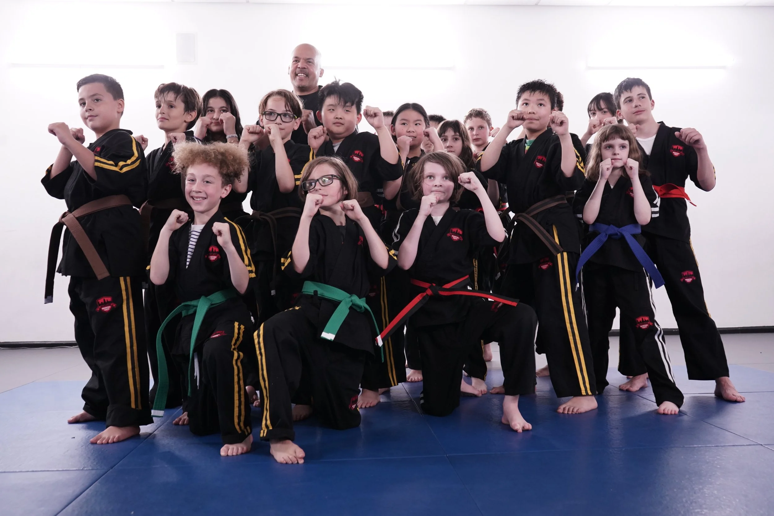 Kids martial arts class group photo with instructor at Modern Martial Arts NYC, students in black belts and colored rank belts