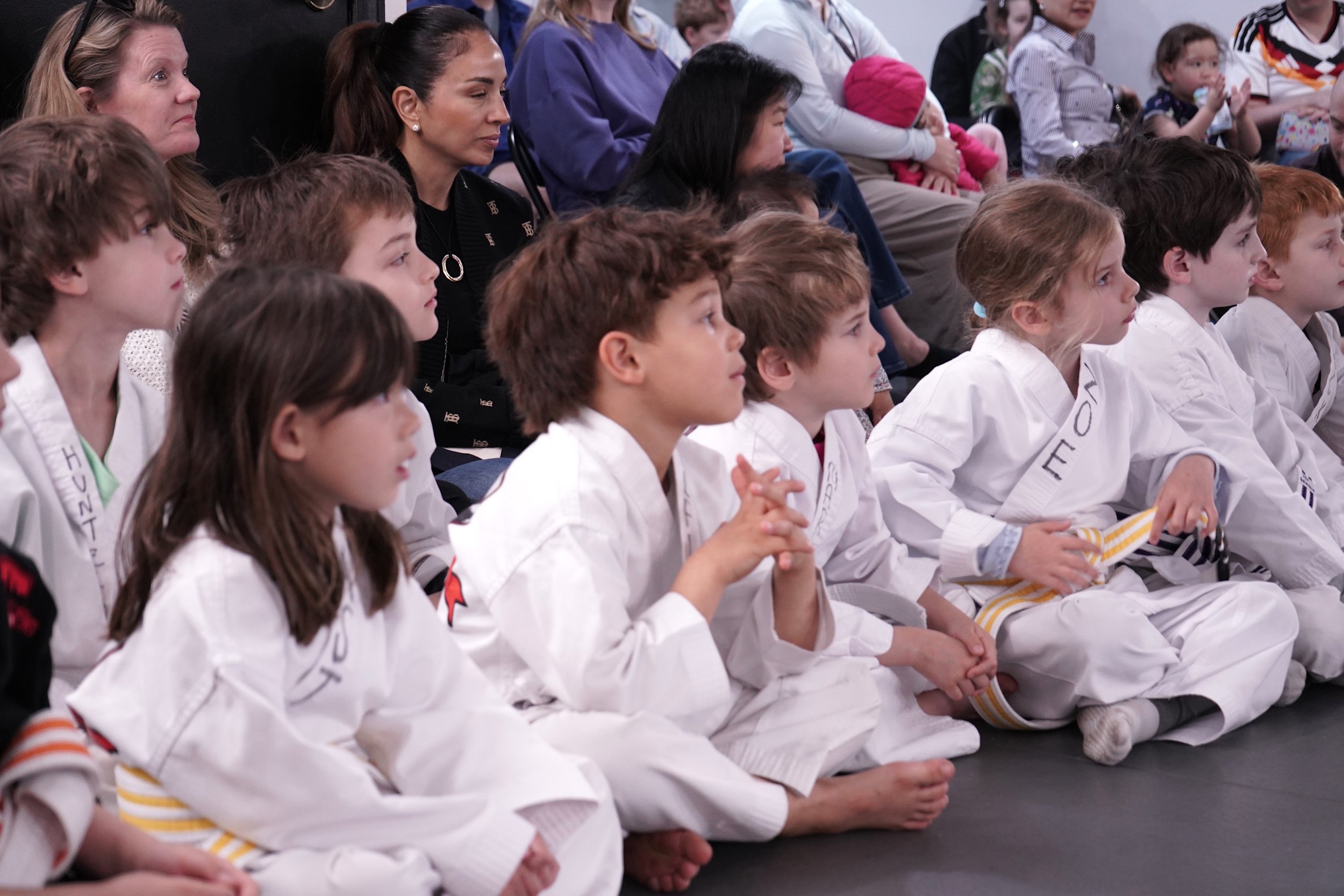 Kids in white karate uniforms sitting attentively during martial arts class in New York City