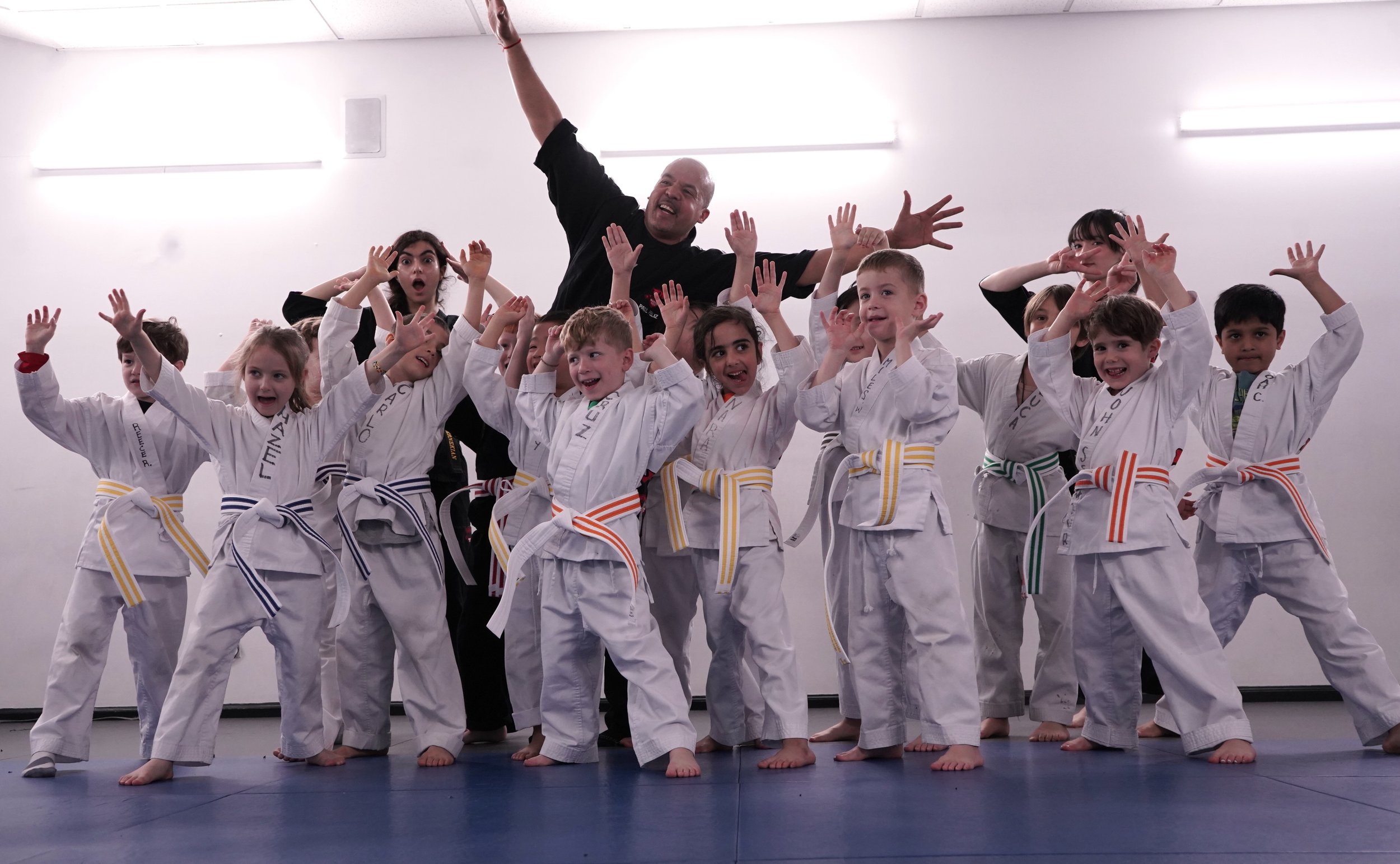 Martial arts instructor celebrating with young white belt students at Modern Martial Arts NYC