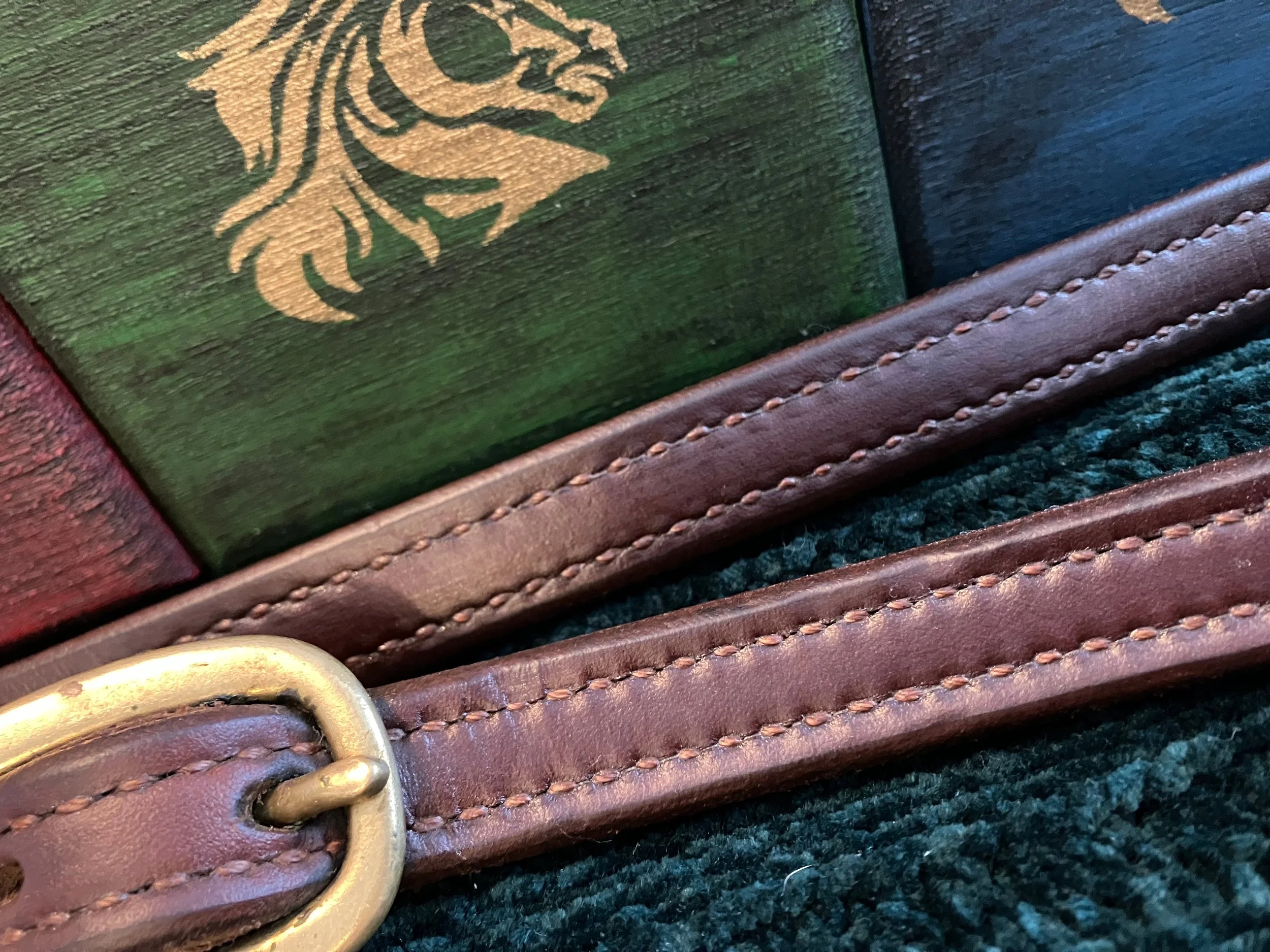 A close up picture of vintage leather halter with brass buckle that has only been cleaned and conditioned with Healthy Leather it's entire life.  The double stitched leather halter looks brand new.  In the background are Healthy Leather's hand painte