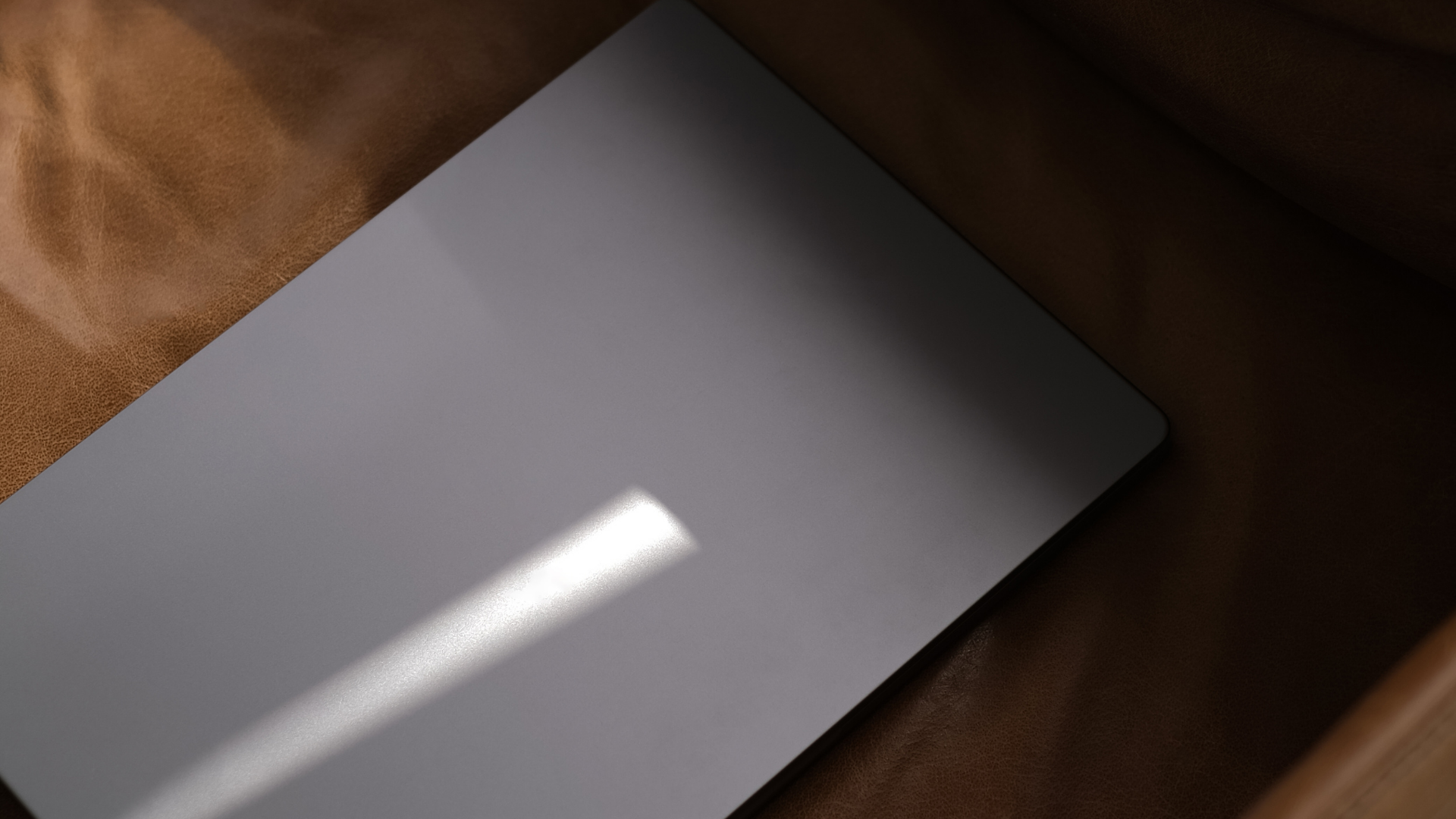 Close-up of a white laptop or tablet with a smooth surface, reflecting light, placed on a brown textured fabric surface.