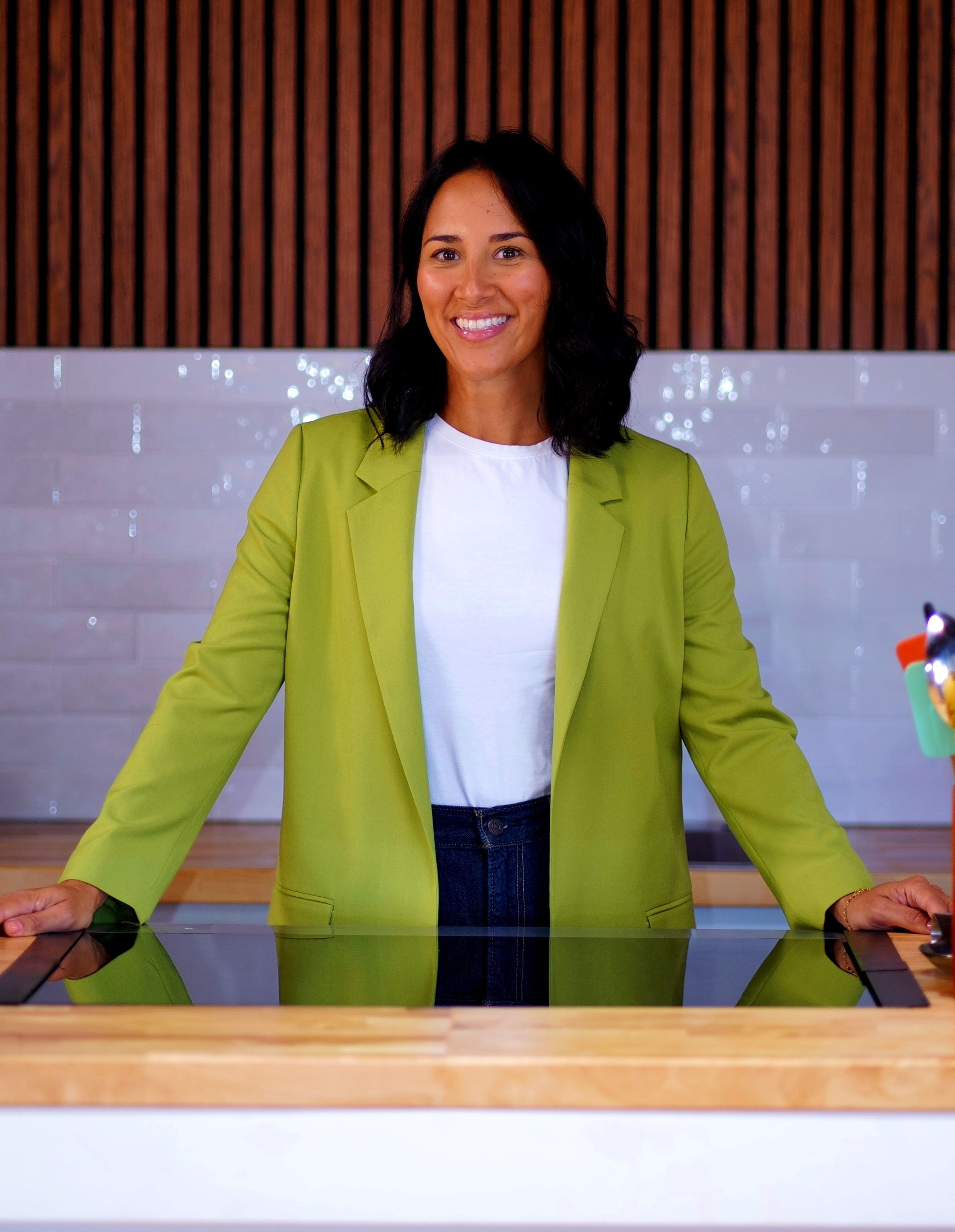 Smiling woman in orange shirt holding a glass of red wine indoors for a company that offers cooking classes and food experiences.