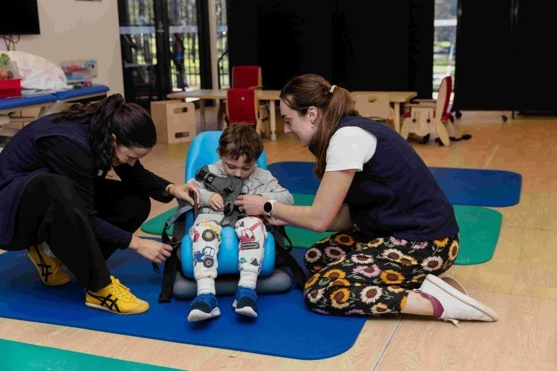 two therapists secure young boy into upright chair