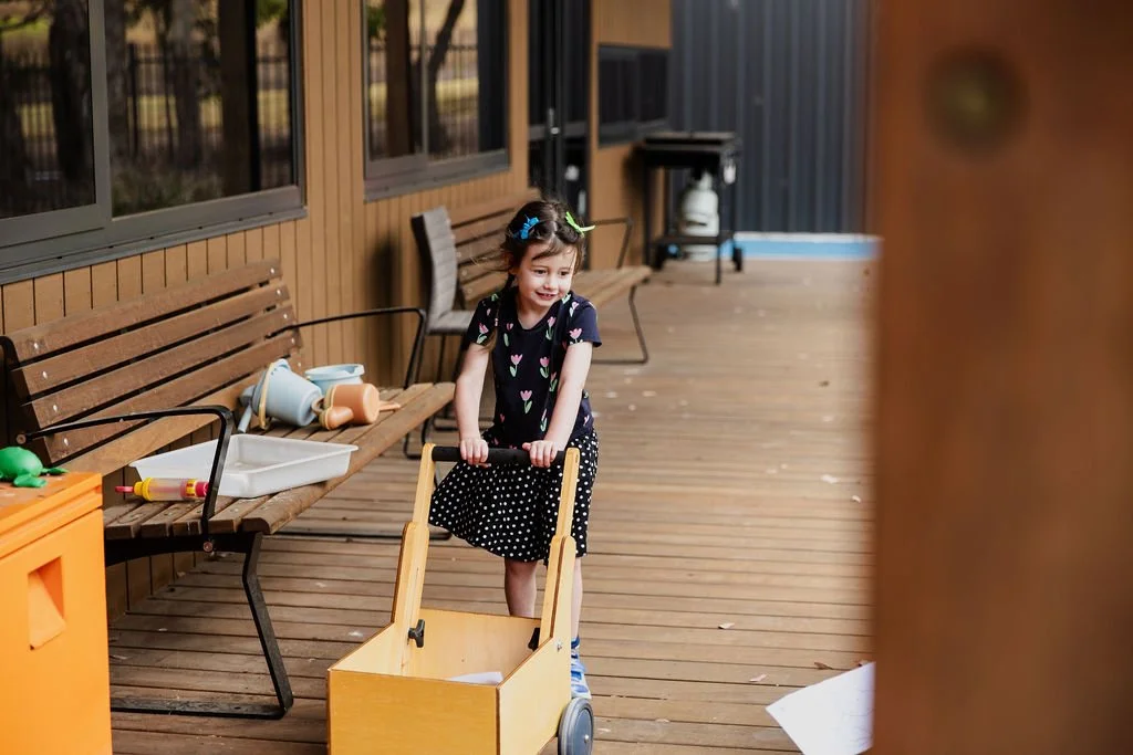 girl in floral dress pushes wooden cart