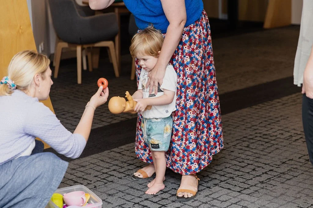 child standing in front of parent is offered a toy during therapy session