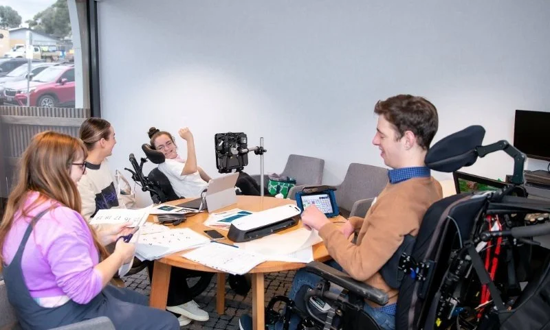 group of people sit around table cutting paper and using aac devices
