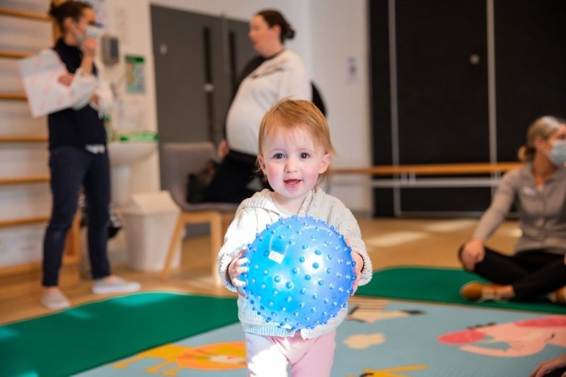 toddler girl smiles at camera as she plays with a large light blue ball