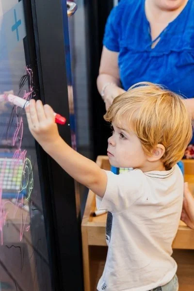 young boy with blonde hair draws on a window with a texter