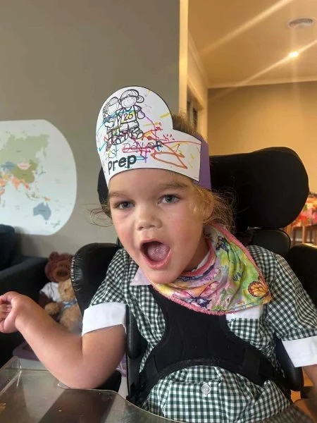 young girl smiles for camera wearing a paper hat that saying 'prep' which has been decorated in colourful texters