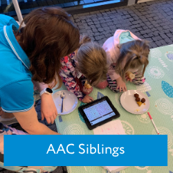 two small children look down at an aac device as an older woman watches on
