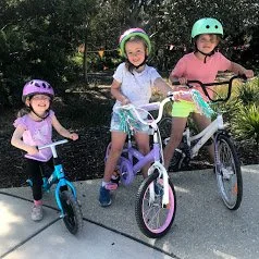 three young girls wearing colourful clothes pose on their bikes