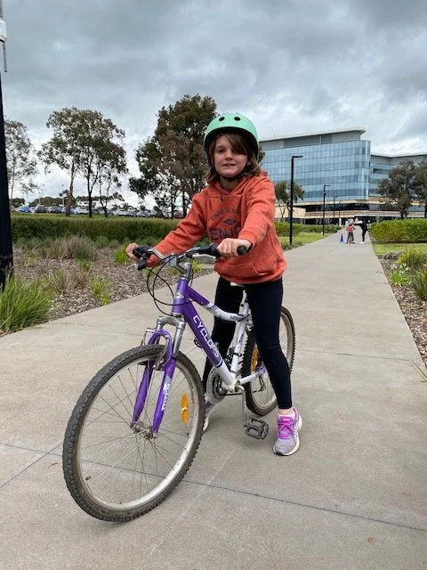 child smiles at camera while riding bike on footpath