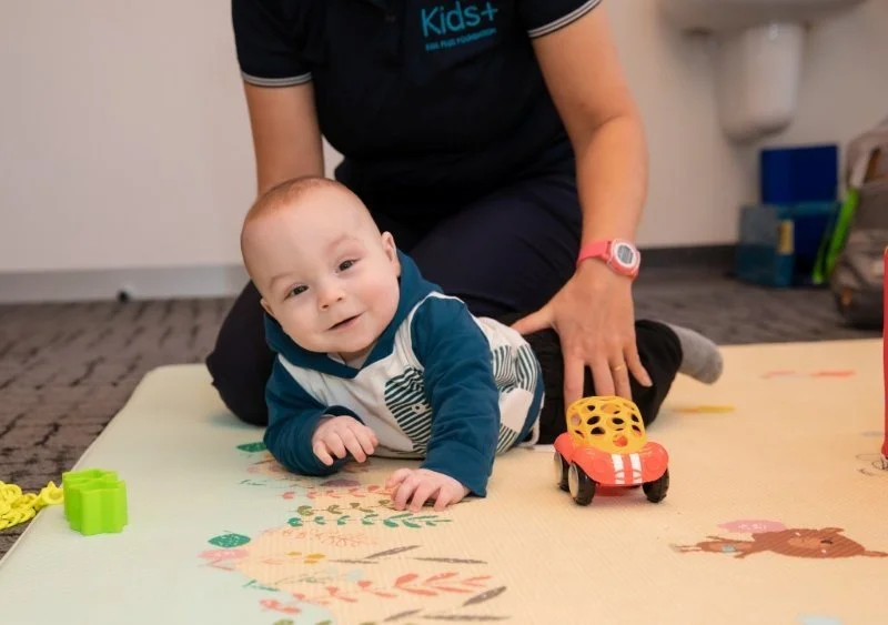 baby gives big smile to camera as he lies on his tummy on a playmat with toys around him