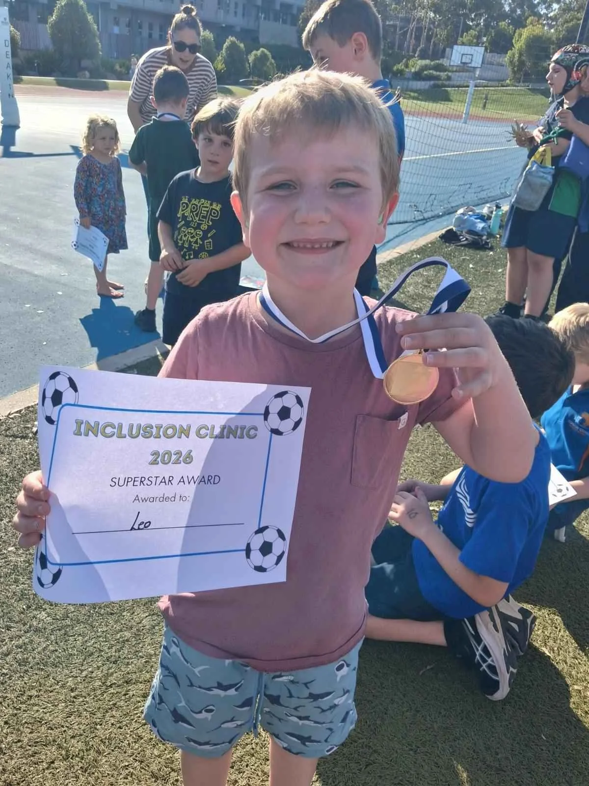 young boys smiles for camera. he is holding a soccer certificate and medal
