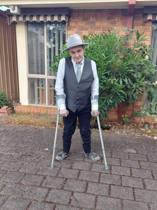 ake Richardson, Kids Plus Scholarship Recipient, wearing a vest, tie and hat, standing with forearm crutches