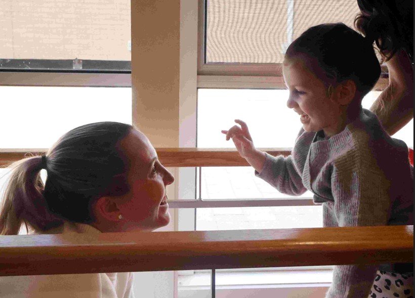 side profile of smiling mother and daughter using wooden balance bars during a therapy session