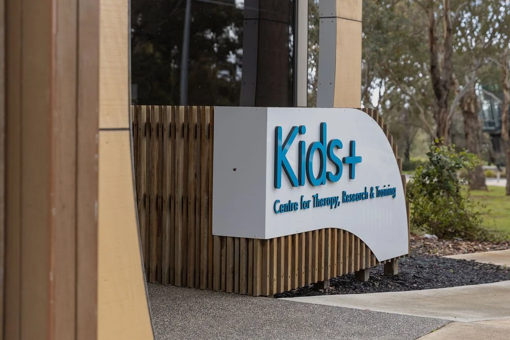 the entrance to the Kids+ foundation which displays a  white sign on a wood, saying 'Kids+, Centre for Therapy, Research & Training'
