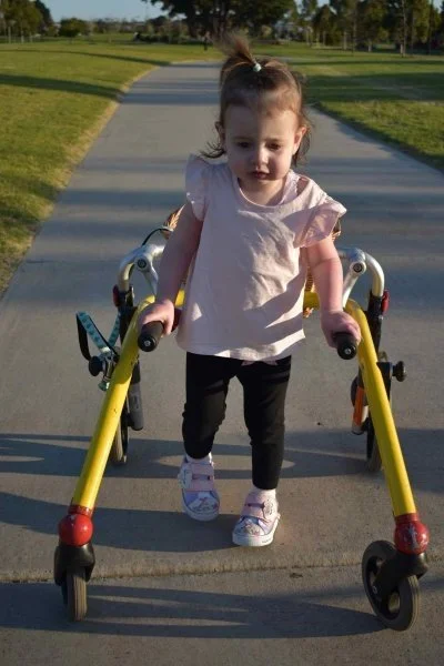 young girl walks outside using a walking frame