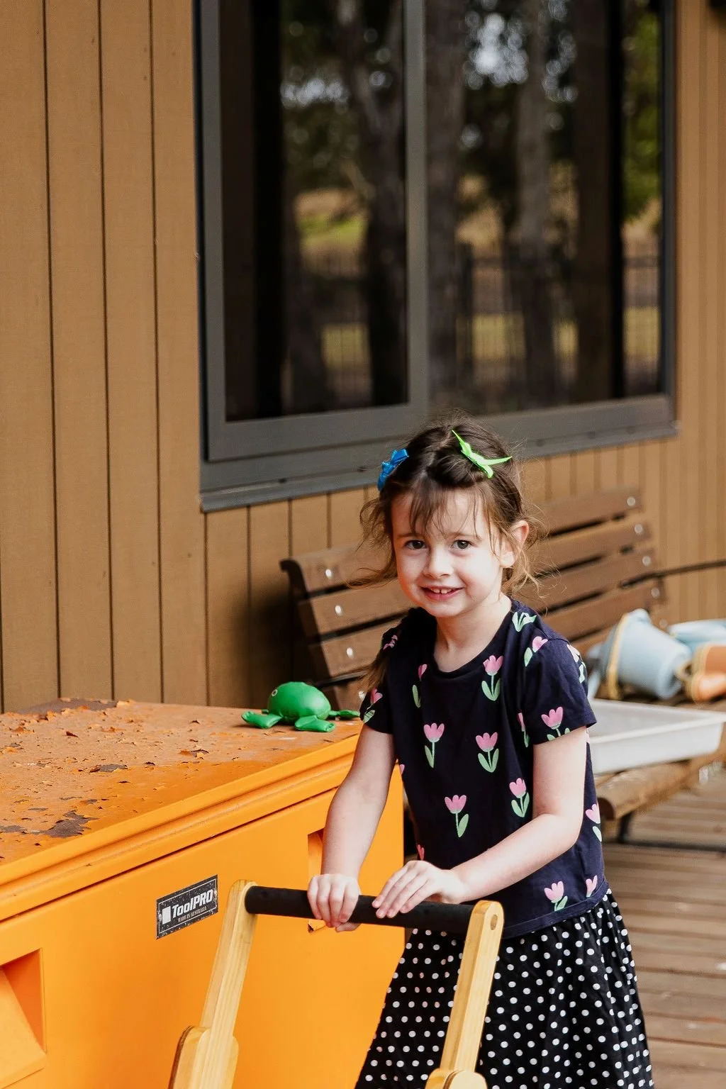 young girl smiles at camera as she pushes a wooden cart