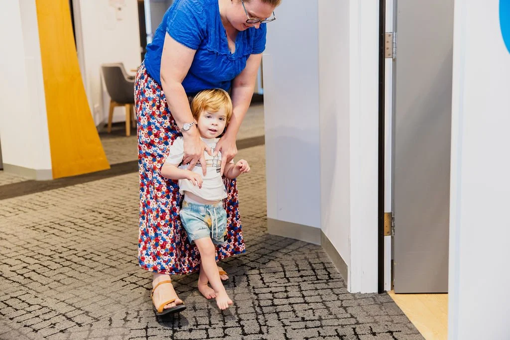 young boy smiles at camera as he is guided gently through a therapy session