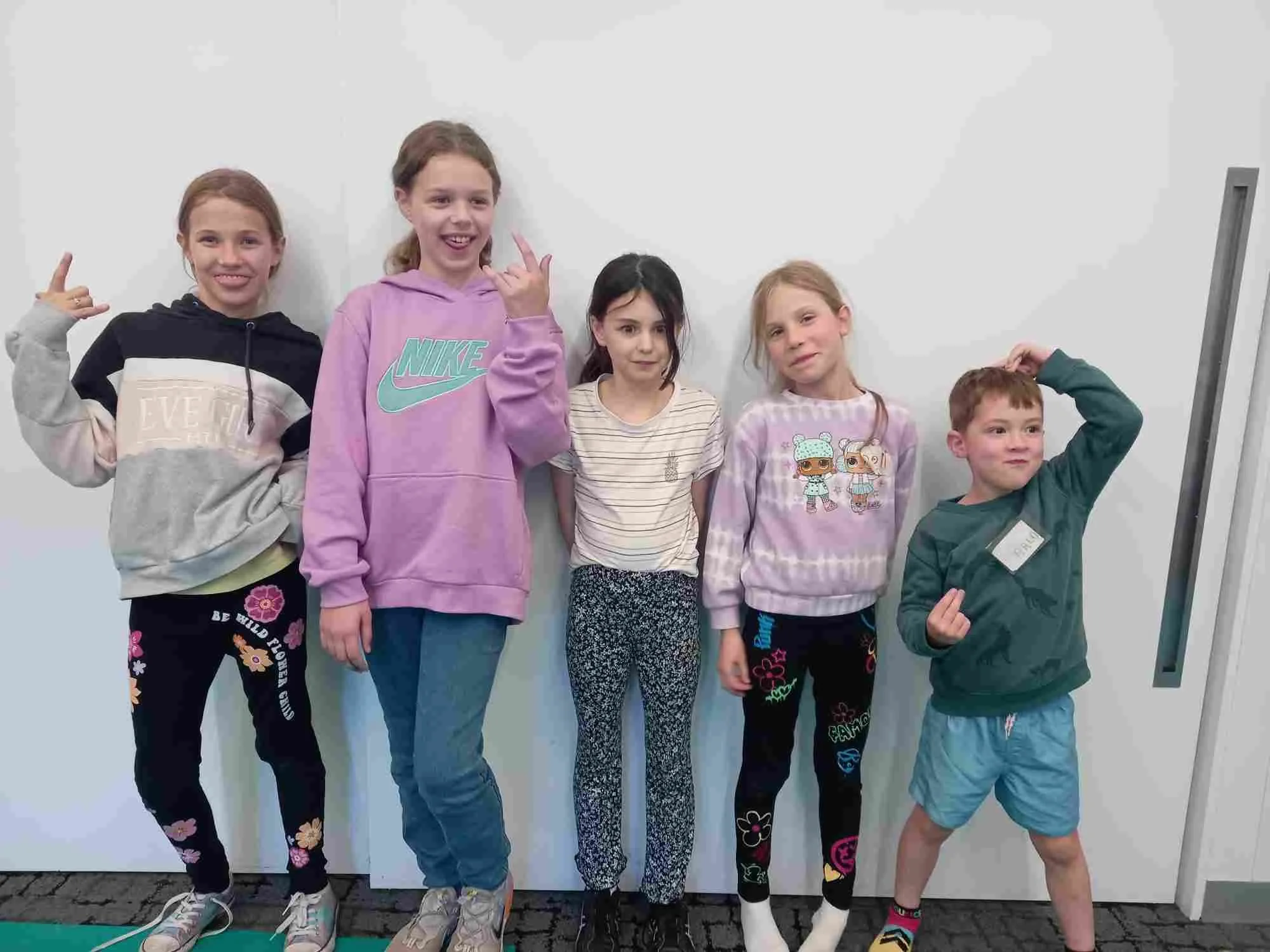 five children of varying ages pose and make silly facing in front of a white wall