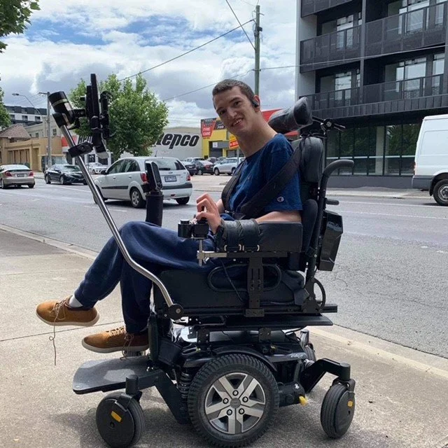 young man in wheelchair smiles at camera on a city street