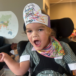 young girl smiles with paper hat on which reads 'Prep'
