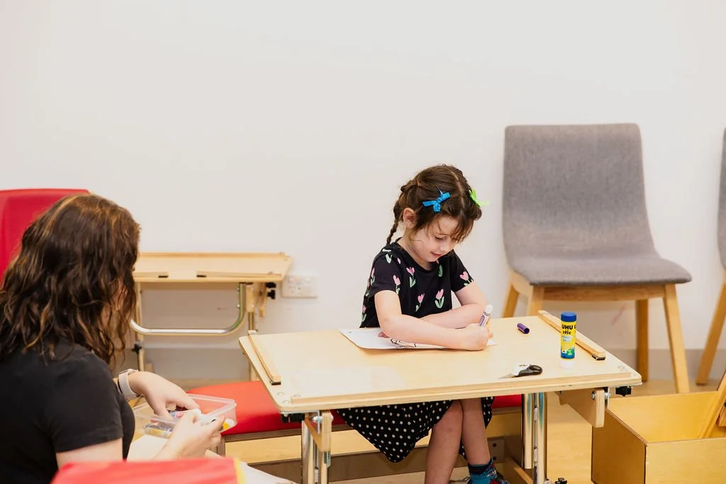 young girl in a speech therapy session at kids plus uses a crayon to draw while sitting at a wooden desk