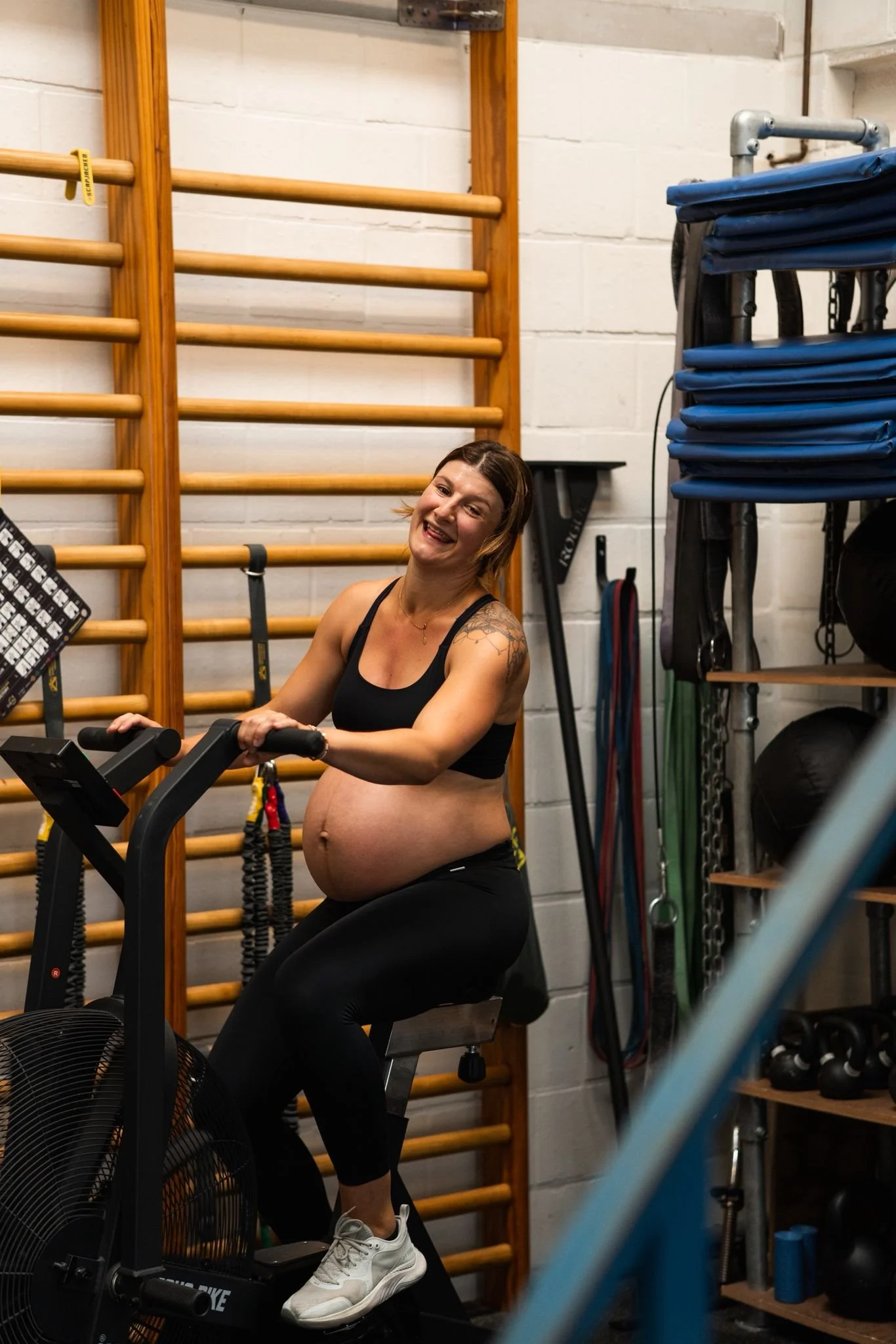 Lachende zwangere atlete op de Airbike tijdens een pre-natale trainingssessie in de box.