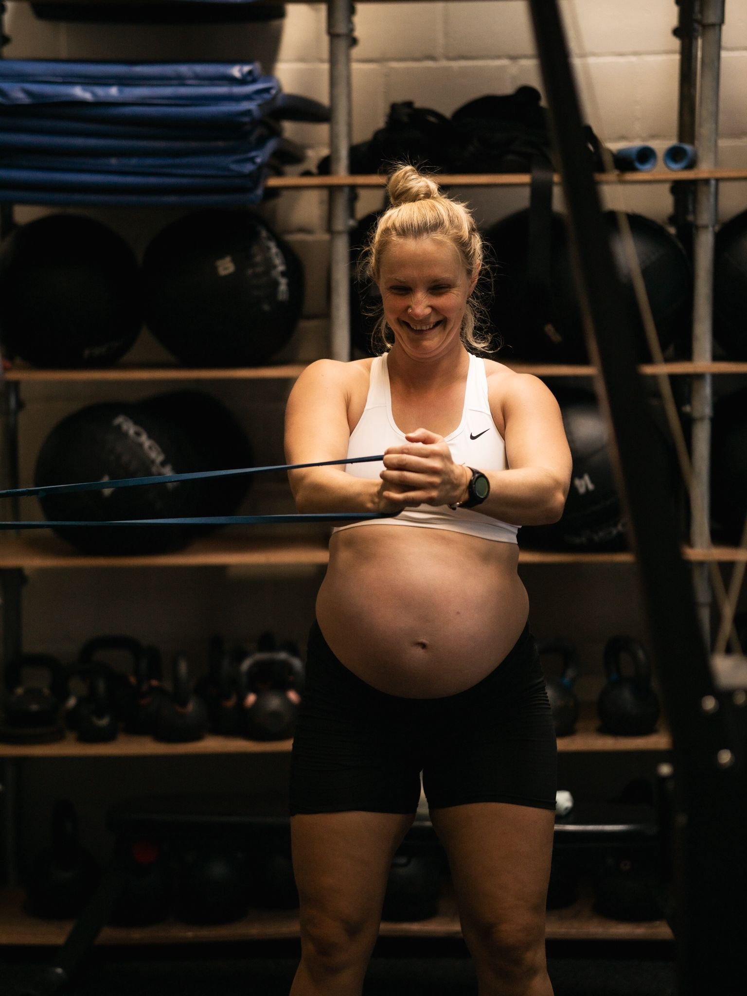 Zwangere vrouw voert lachend een gecontroleerde oefening met een weerstandsband uit bij Black Oak CrossFit Turnhout.