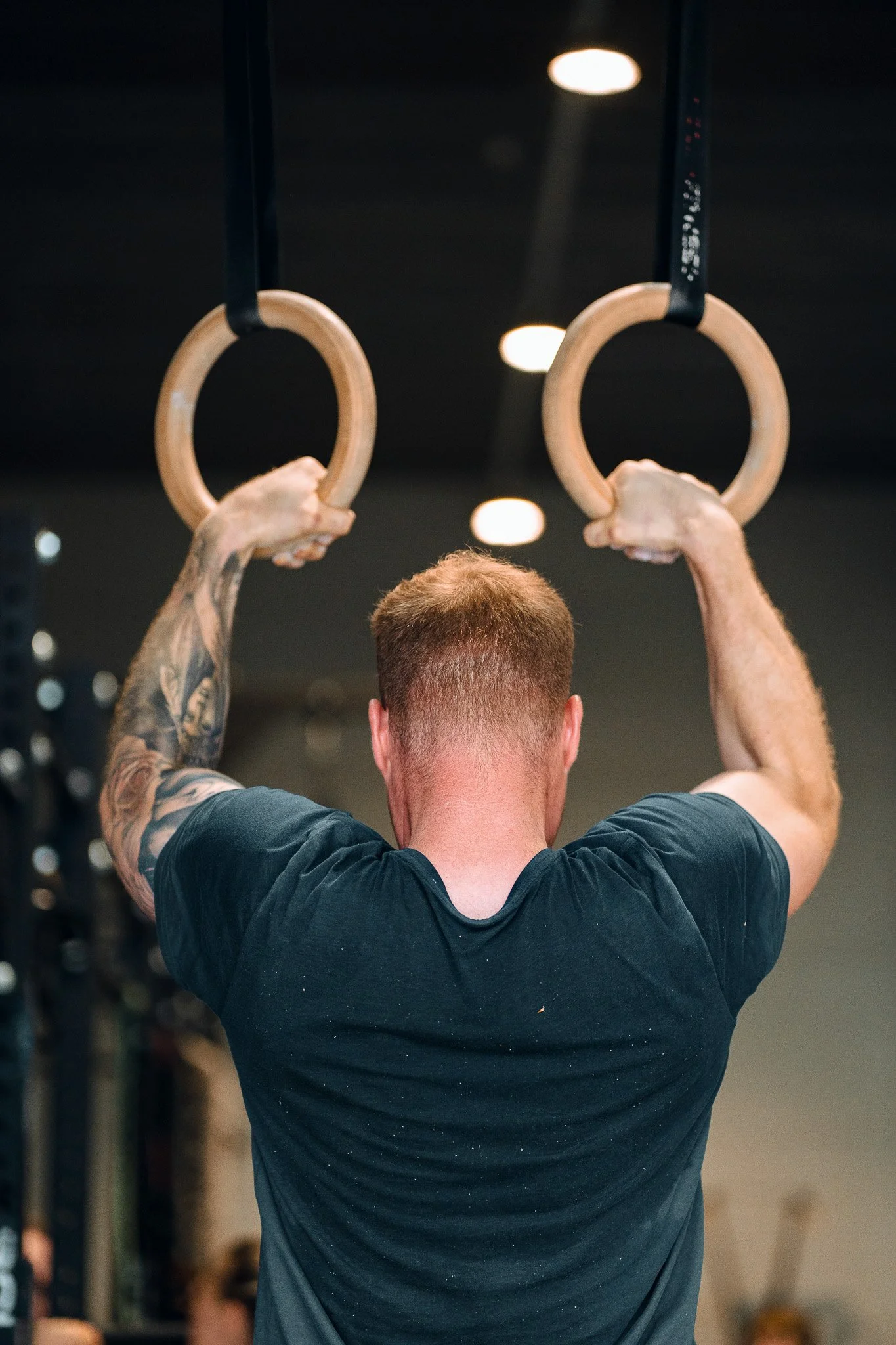 Atleet met getatoeëerde arm bereidt zich voor op een ring workout tijdens een Gymnastics les bij Black Oak.