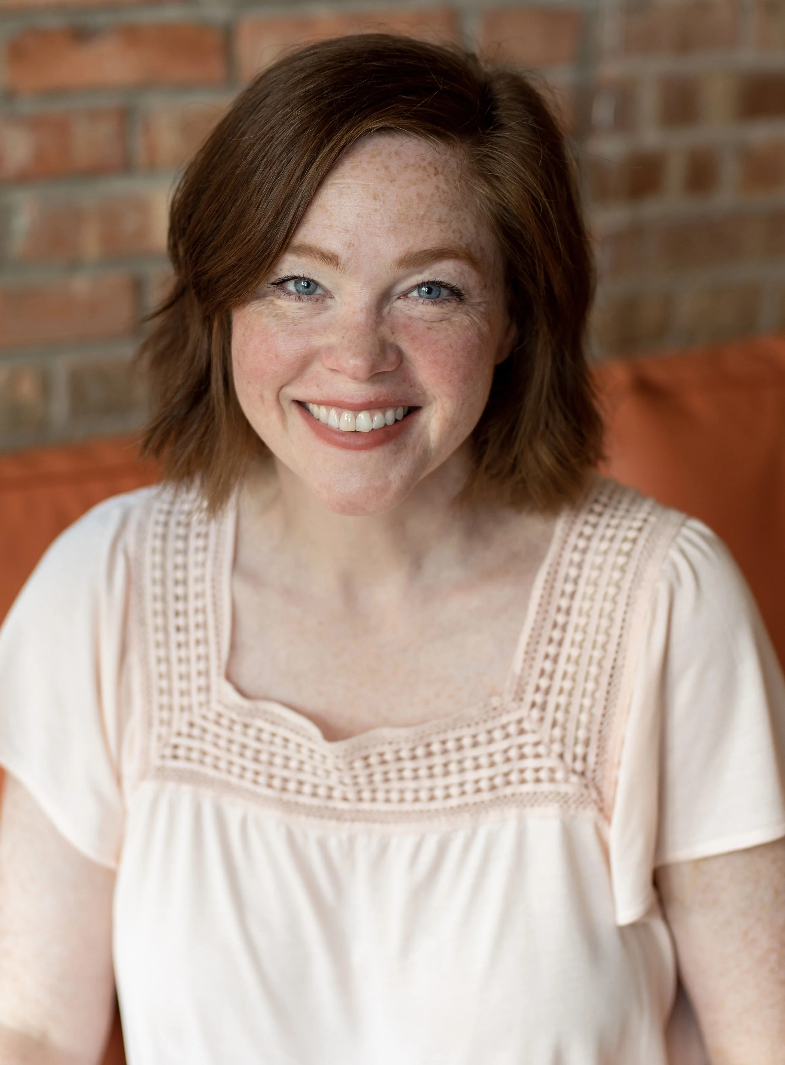 A smiling woman with shoulder length red hair and freckles.