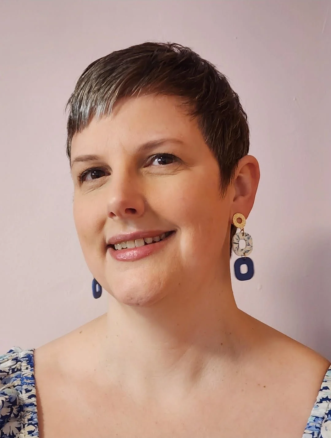 A woman with a pixie haircut and dangling earrings smiles into the camera