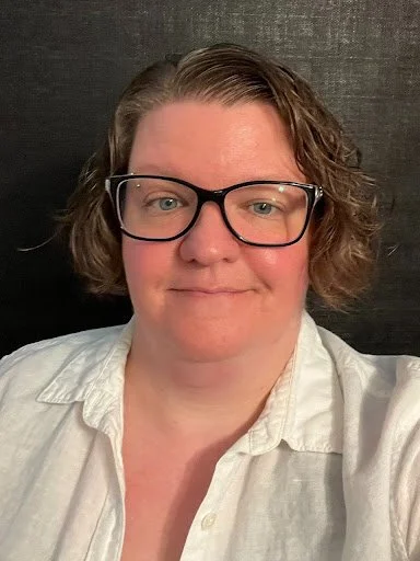 Woman with short brown hair, black-framed glasses, and a white blouse smiles at the camera. 