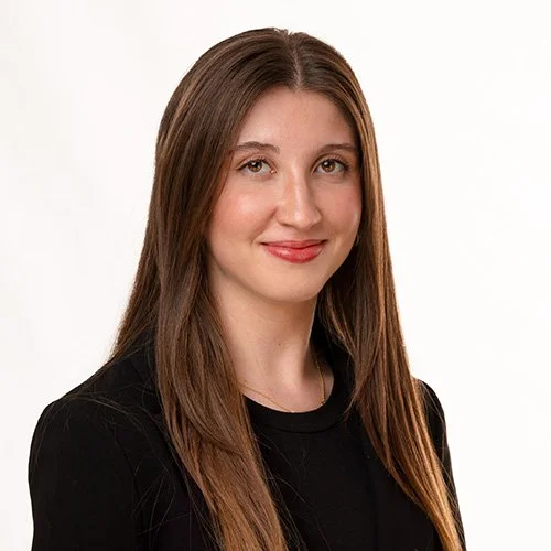 A headshot of a woman in a dark top with brown hair on a white background