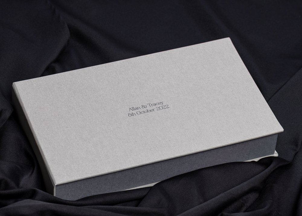 A rectangular grey print box resting on black fabric, with personalised text on the lid.