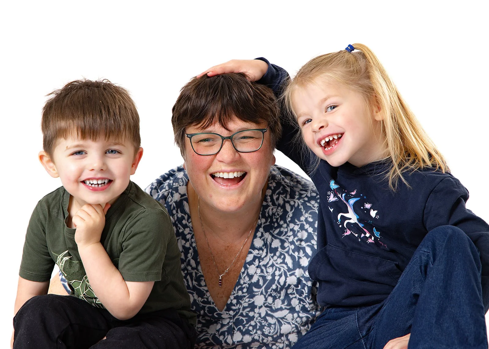 A woman with short brown hair and glasses, smiling, with two young children, a boy and a girl, all smiling happily against a white background.
