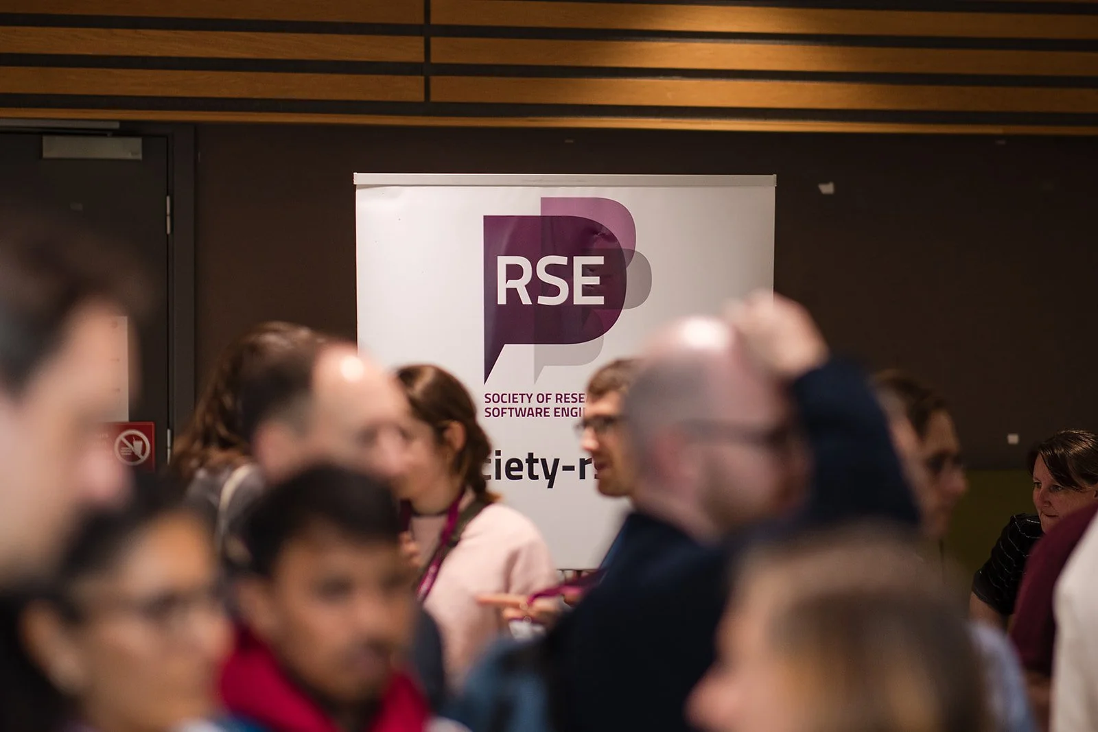Group of people at a conference or event, with a focus on a banner in the background that reads 'Society of Research Software Engineers'.