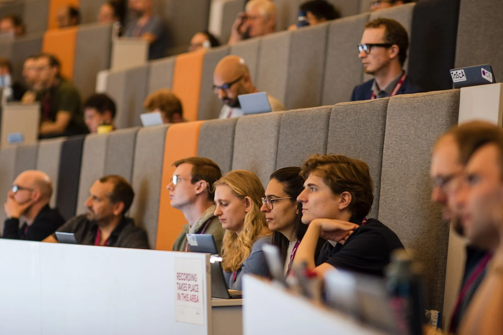 People attending a conference or seminar seated in an auditorium, listening attentively.