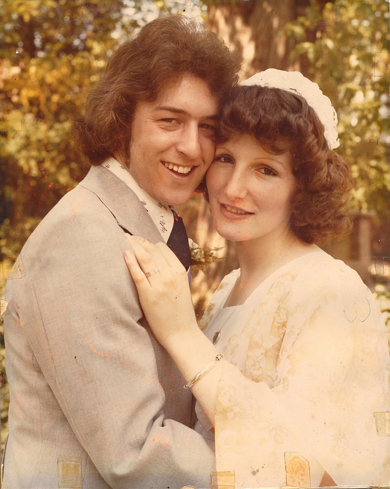 A vintage photo of a smiling couple embracing outdoors with autumn trees in the background.