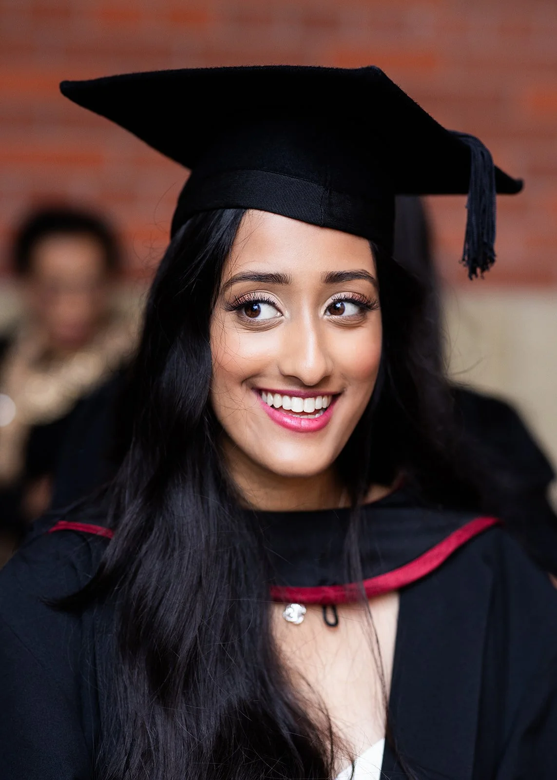 A young woman wearing a black graduation cap and gown, smiling at a graduation ceremony.