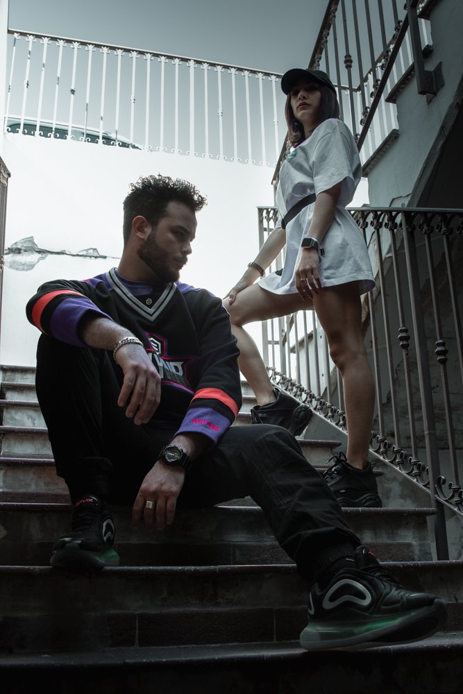 Due persone sedute e in piedi su una scala di marmo all'aperto con ringhiera di ferro, sotto un cielo nuvoloso.