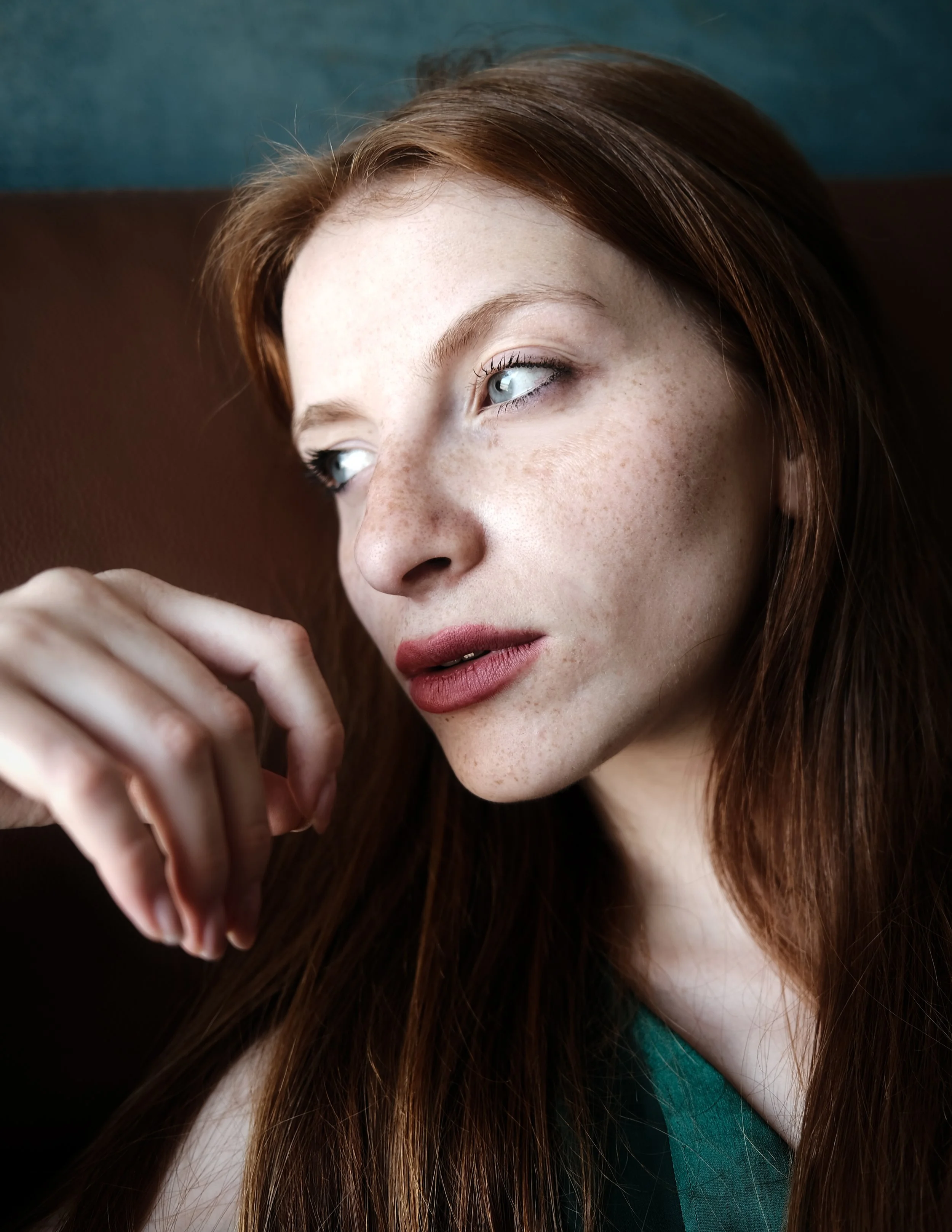 Ragazza dai capelli castani con lentiggini, che guarda verso sinistra, con sfondo scuro e luci naturali.